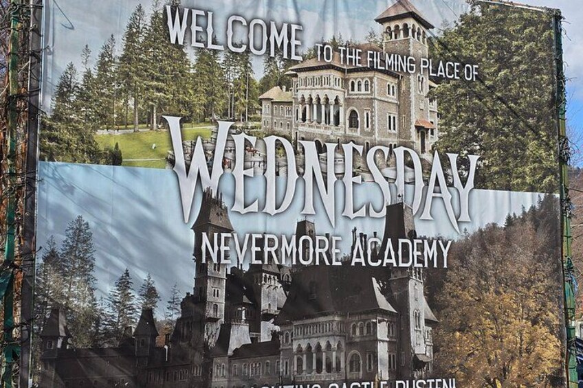 A sign welcoming visitors to the filming location of 'Wednesday Nevermore Academy' with a castle-like building in the background. 2