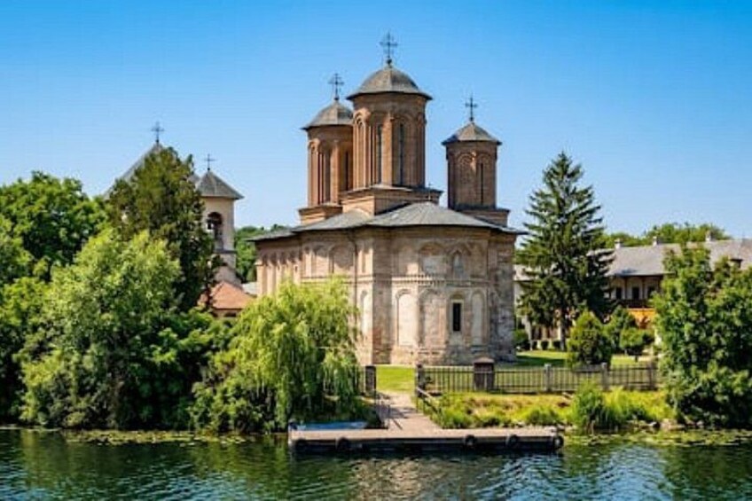 A historic church with a central dome and two smaller domes, surrounded by lush greenery and a calm body of water. 2