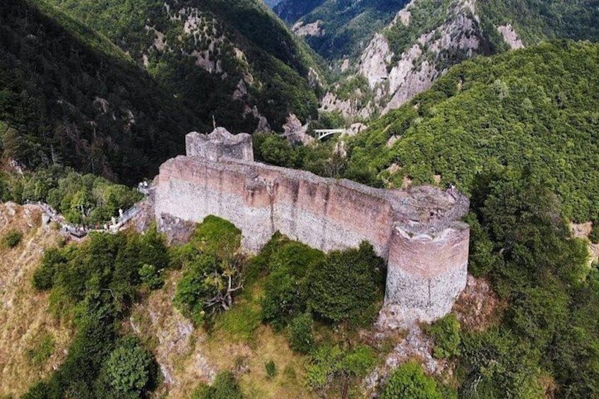Eine große, altehrwürdige Steinburg, umgeben von üppigen grünen Hügeln. 1