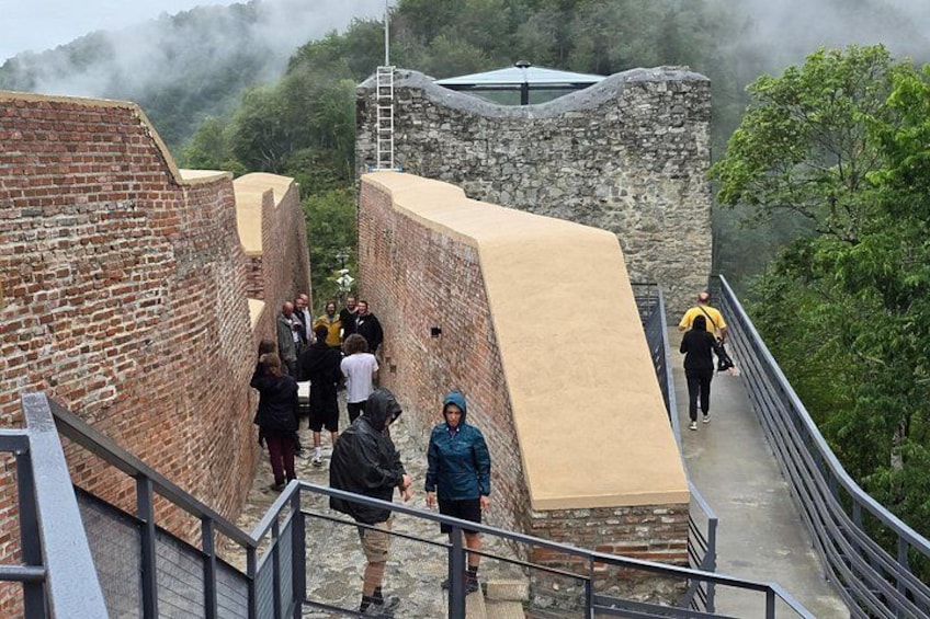 Eine Gruppe von Menschen geht über eine Steinbrücke, an deren Seite eine Backsteinmauer steht. 2