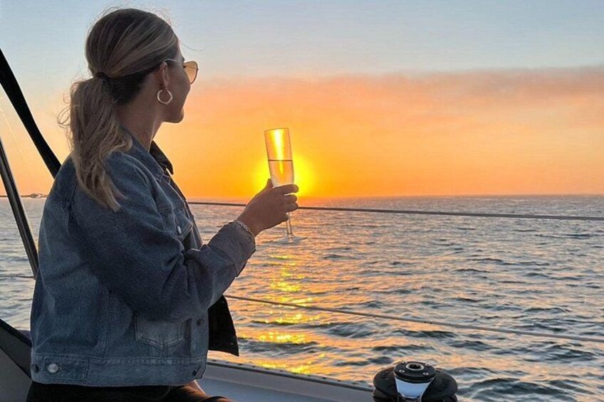 Una persona sosteniendo un vaso, un barco y una puesta de sol sobre el agua. 4