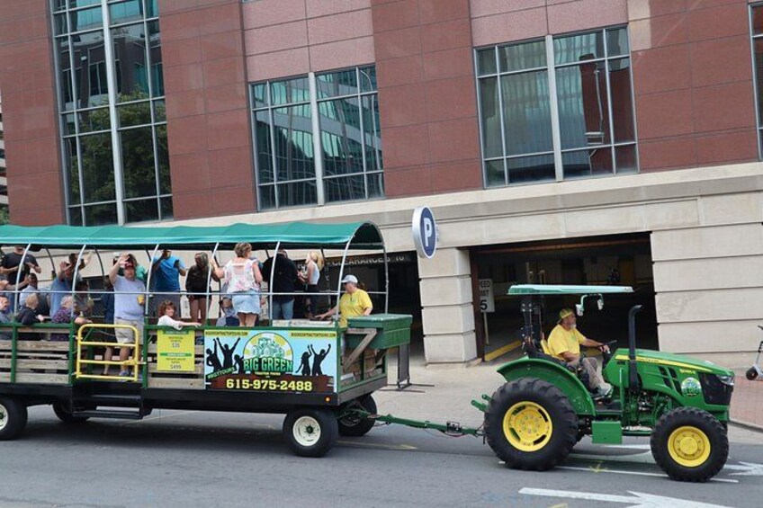 Ein grüner Traktor zieht einen Personenwagen mit Personen, der vor einem Gebäude mit blauem Parkschild steht. 4
