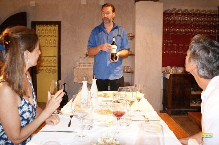 A dining table with wine glasses, bottles, and a person holding a bottle. 4