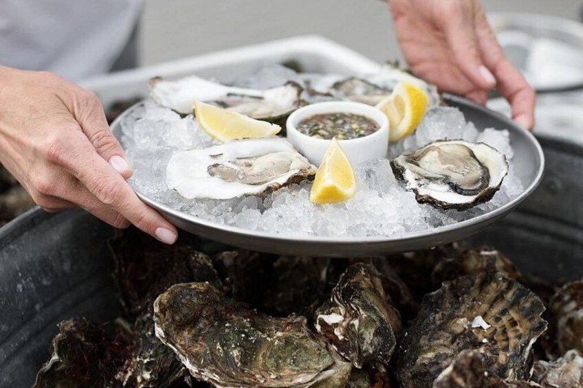 Een persoon houdt een bord met oesters op ijs vast, met partjes citroen en dipsaus erbij. 5