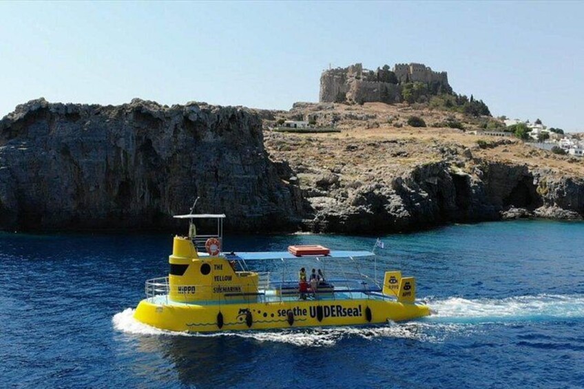 Een gele boot genaamd 'The Yellow Submarine' met 'The Undersea' op de zijkant, vaart langs rotsachtige kliffen en een kasteel op de achtergrond. 4
