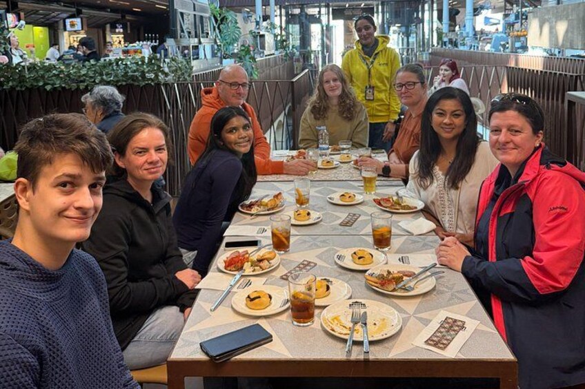 A group of people seated around a table with food and drinks, in a public indoor space with a modern design. 3