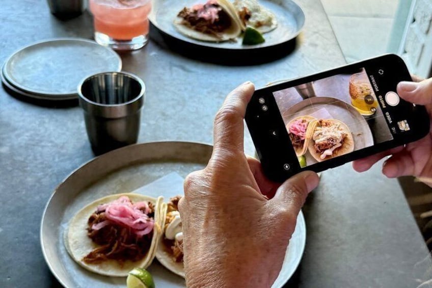En person håller i en smartphone och tar ett foto av en tallrik med tacos. 3
