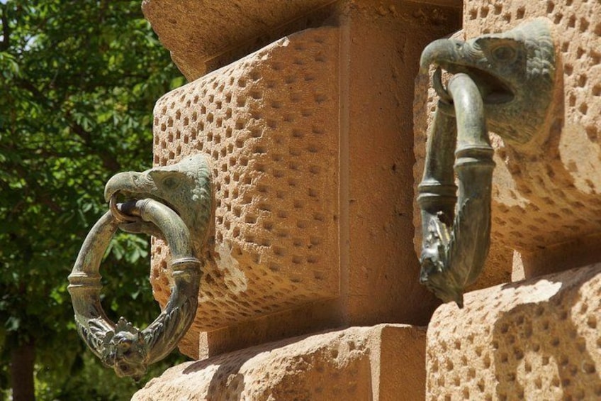 A close-up of a textured stone structure with two metal handles, one shaped like a ring and the other a traditional faucet. 3