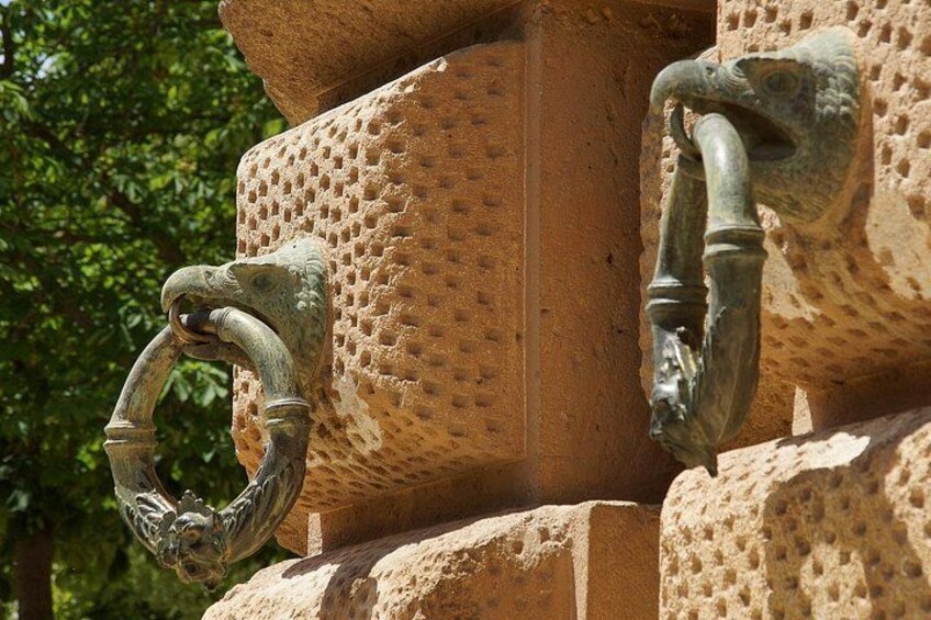 A close-up of a stone structure with a textured surface and two metal handles, one shaped like a ring and the other a curved pipe. 4