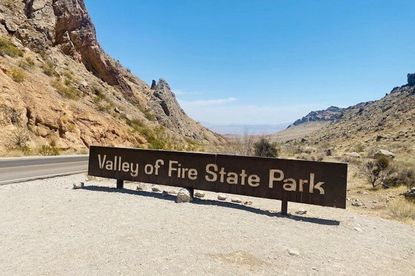 A sign for Valley of Fire State Park with a road in the background. 4