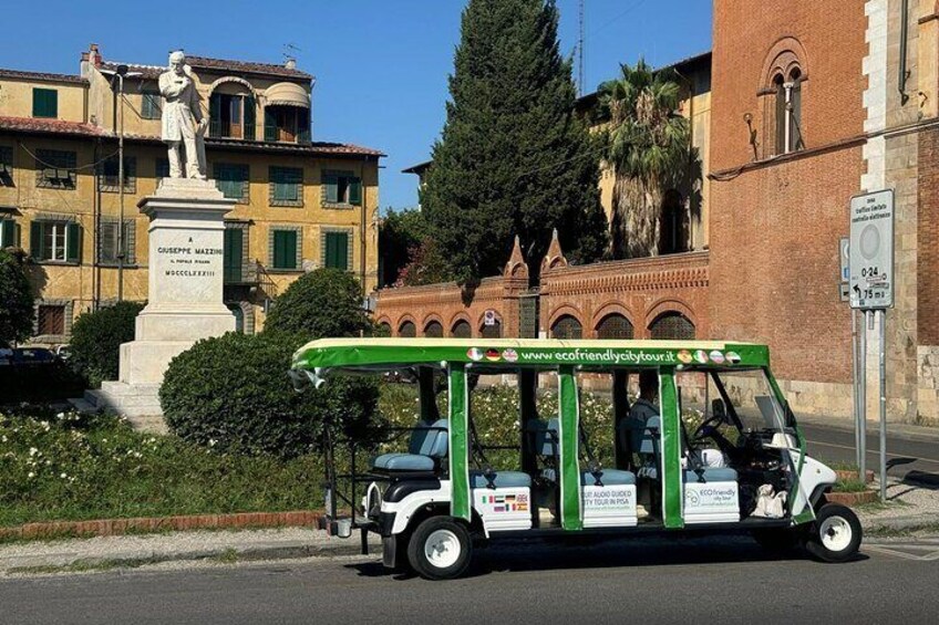 Carro de golf eléctrico verde y blanco estacionado en una calle, con una estatua y un edificio al fondo. 1