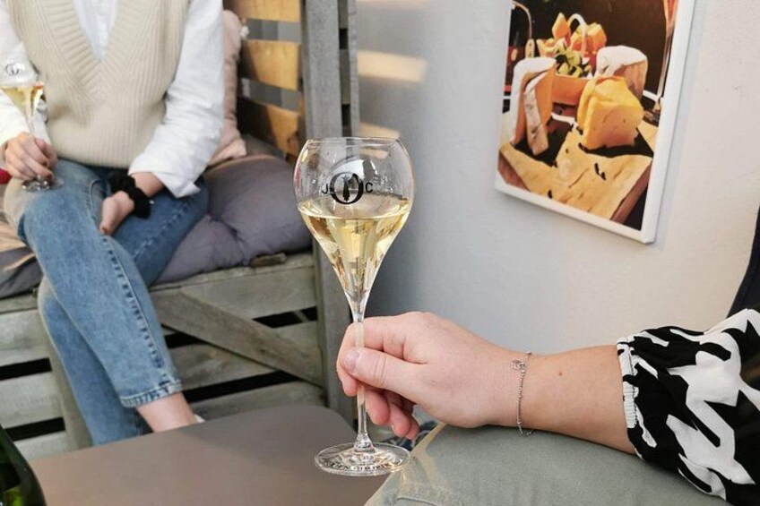 Una persona che tiene un bicchiere di vino, seduta a un tavolo con un cuscino e un quadro appeso al muro. 2