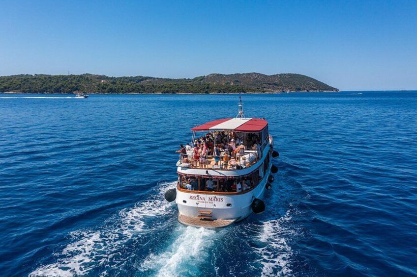 A white and red boat with passengers, moving on a blue sea with a distant green landmass. 3