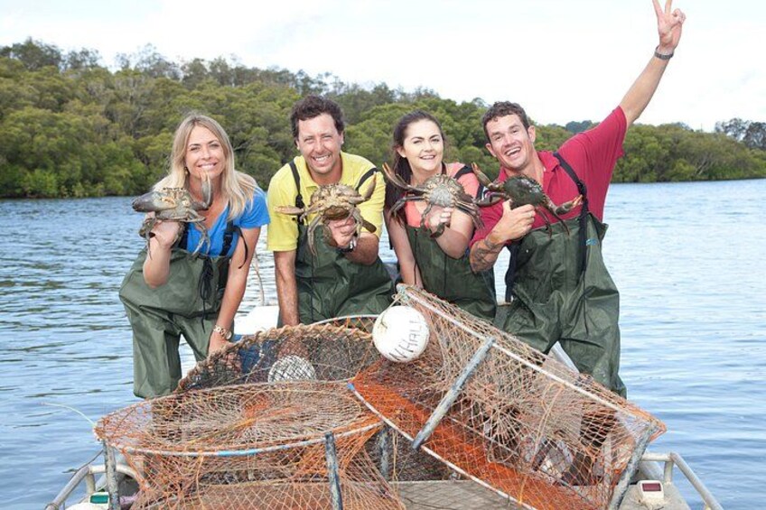Four people on a boat holding crabs, with a net and a fishing rod visible. 1