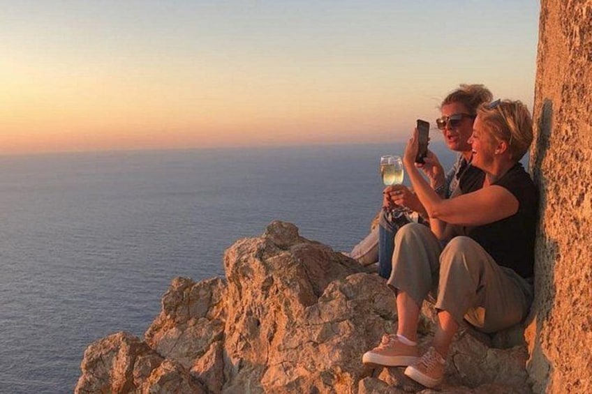 Deux personnes assises sur un promontoire rocheux au bord de la mer, au coucher du soleil. 2