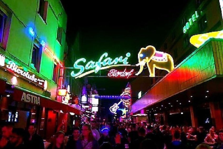 A brightly lit street with neon signs, including 'Safari' and 'Astra'. 1