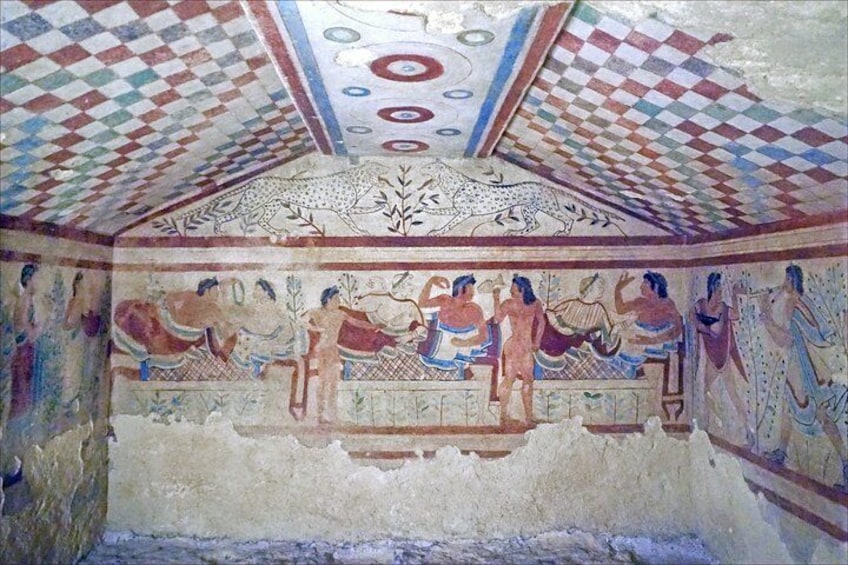 A fresco with geometric patterns on the ceiling and a scene of people in ancient attire on the wall. 3