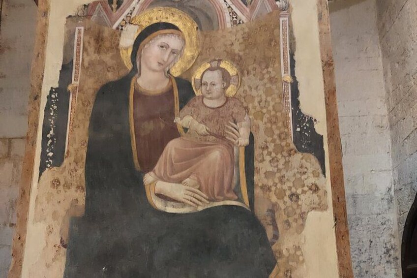 Affresco con una figura centrale che tiene un bambino, circondato da elementi decorativi. 2