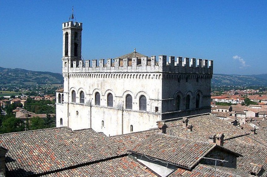 Un edificio storico con una torre e finestre ad arco, immerso in un paesaggio collinare. 1