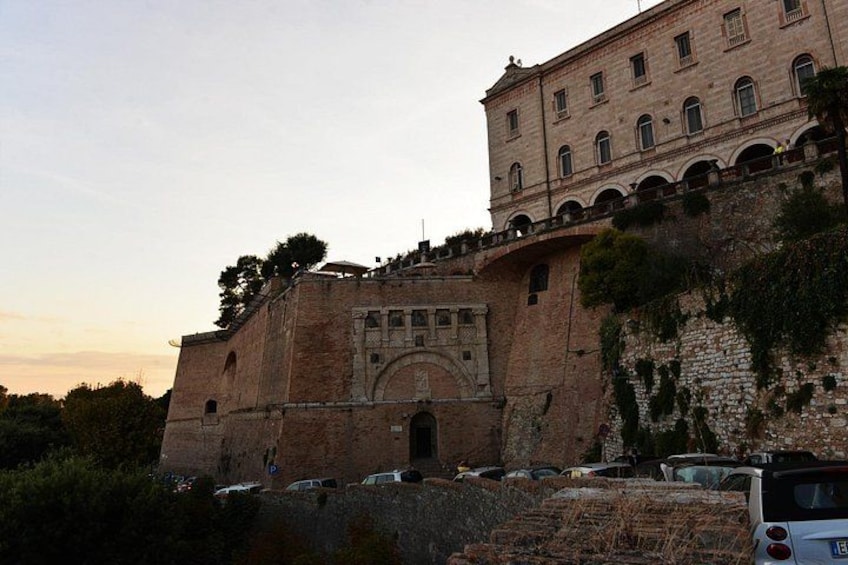 A historic building with arched windows and a stone facade, surrounded by trees and parked cars. 1