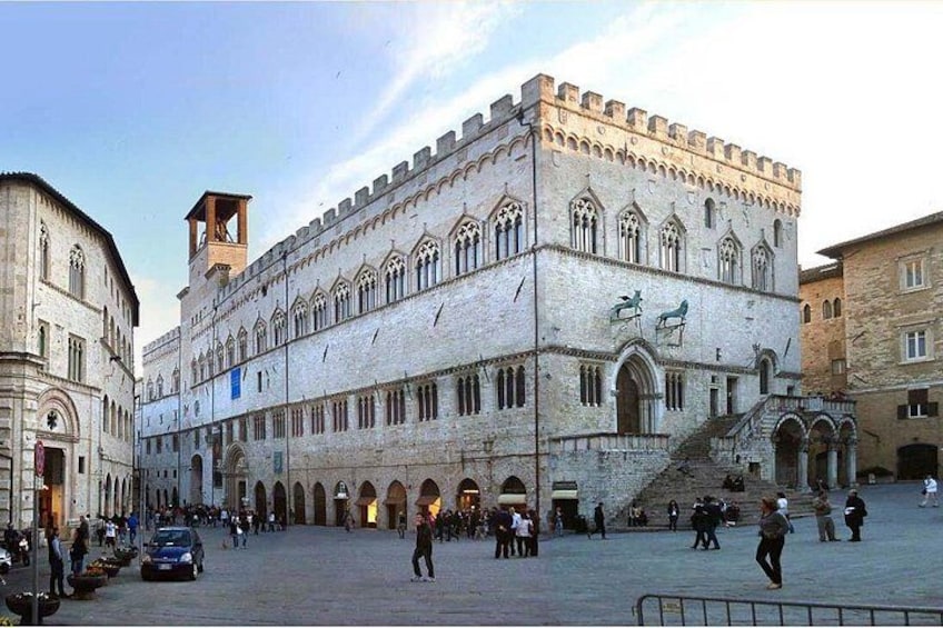 A historic building with a tower, arched windows, and a courtyard with people and cars. 2