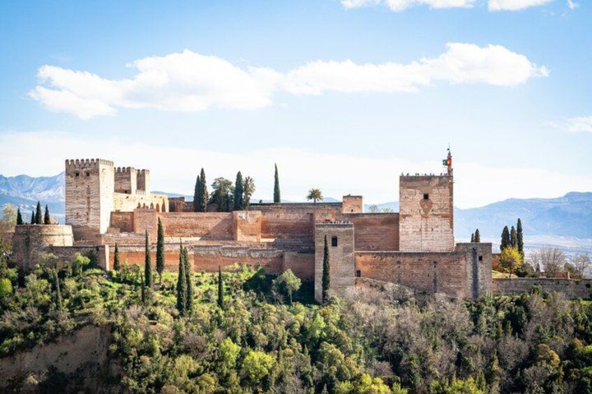 A historic fortress with multiple towers and walls, surrounded by a forested landscape and mountains in the background. 3
