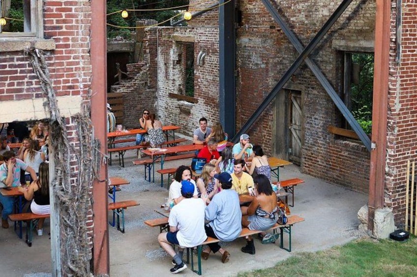 A group of people seated at outdoor tables in an industrial-style setting with brick walls and metal beams. 5