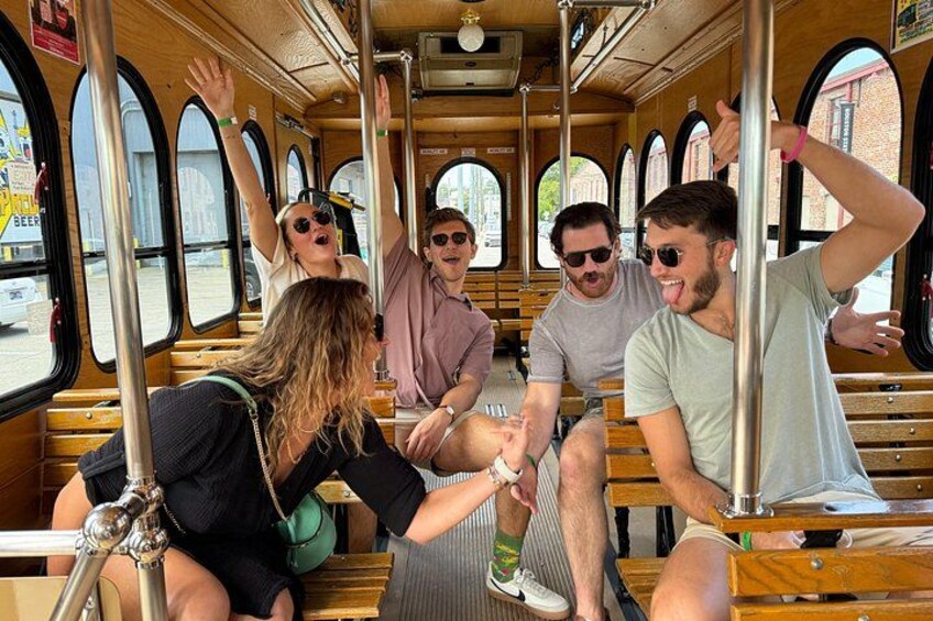 A group of people on a bus with large windows and wooden seats. 3