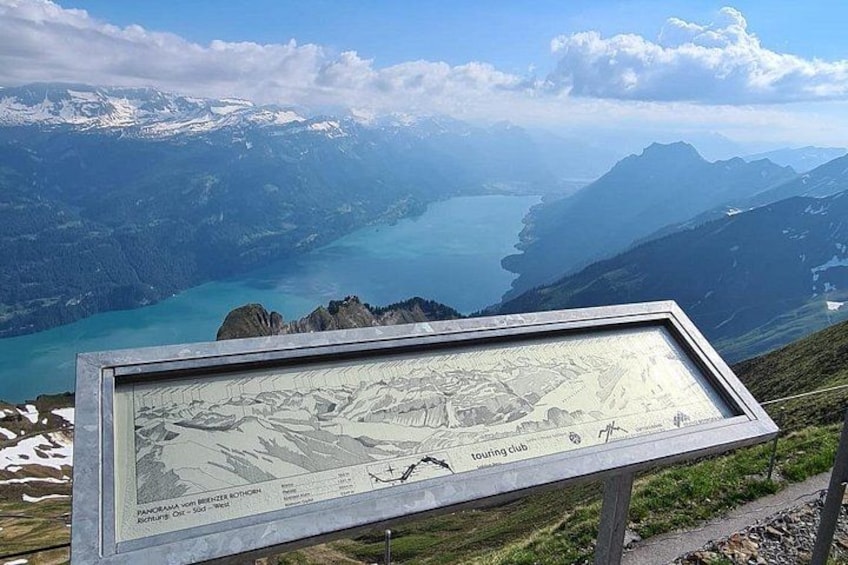 A mountain landscape with a lake, a hiking trail, and a signboard. 3