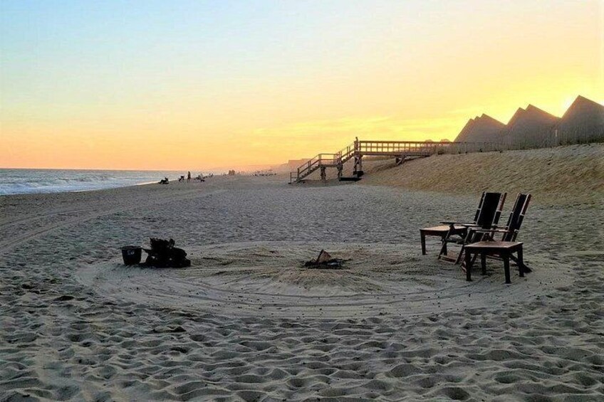 A beach with a fire pit, chairs, and a wooden walkway leading to a structure. 4