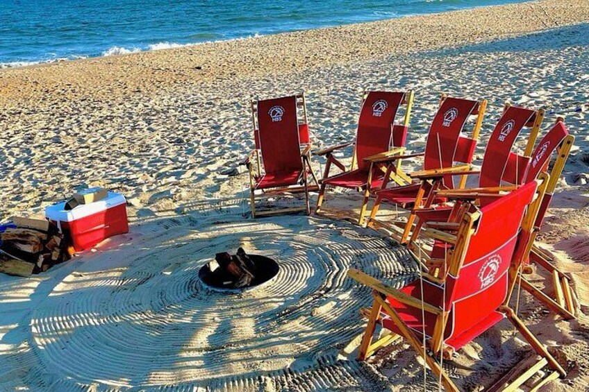 A beach with red Adirondack chairs arranged in a circle, a cooler, and a hat on the sand. 5