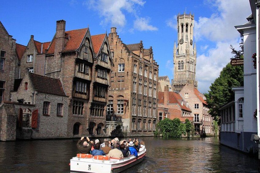 A boat with passengers on a canal, historic buildings, and a tower in the background. 3