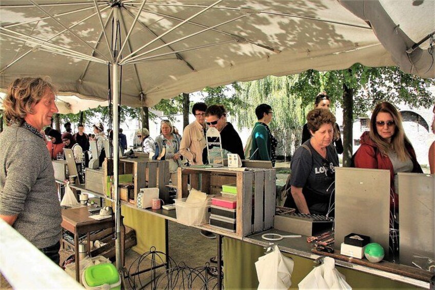 An outdoor market with people standing at stalls under umbrellas. 2