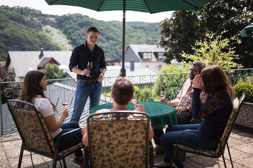 Un groupe de personnes est assis à une table en plein air, et un homme se tient debout à côté, tenant un verre de vin. 3