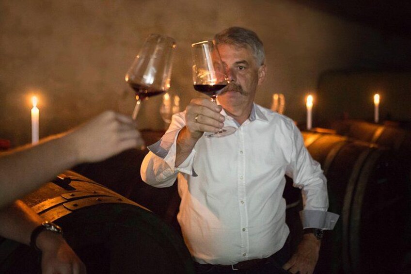 Une personne tenant un verre de vin dans une pièce faiblement éclairée, où sont allumées des bougies. 2