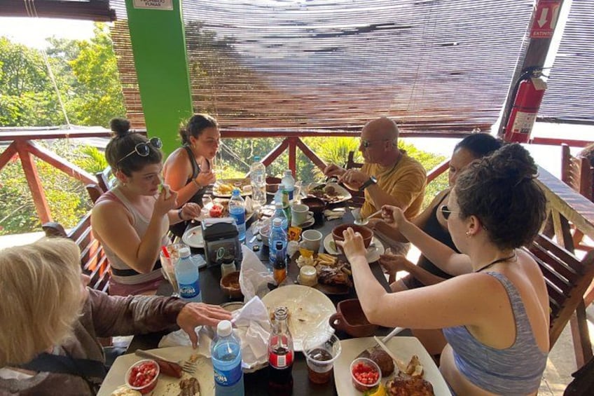 A group of people dining at an outdoor table with various dishes and drinks. 3