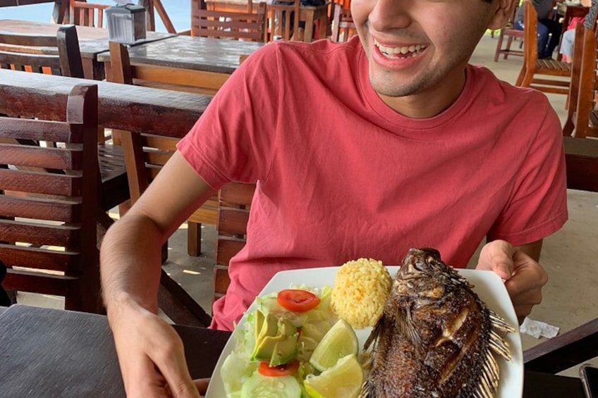 A person seated at a wooden table with a plate of food, including a whole fish, rice, and vegetables. 4