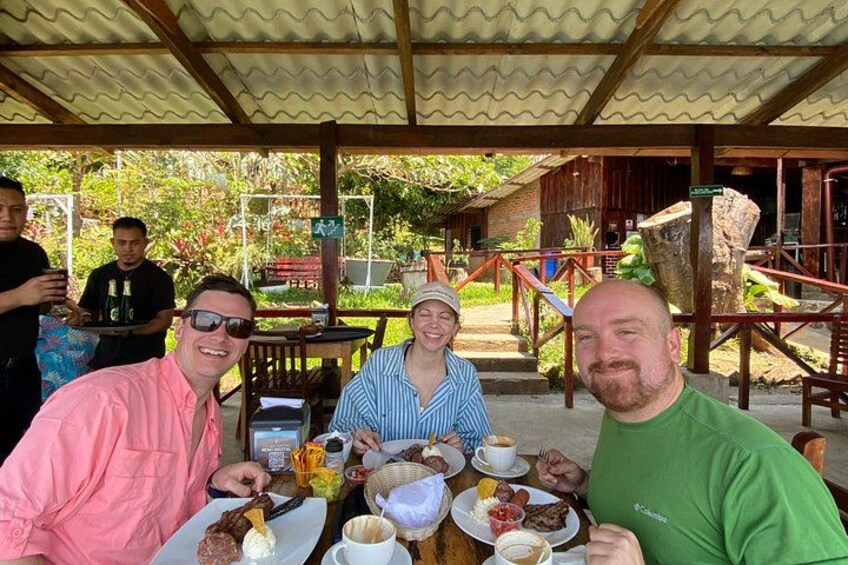 A group of people dining outdoors at a wooden table with various dishes and drinks. 5