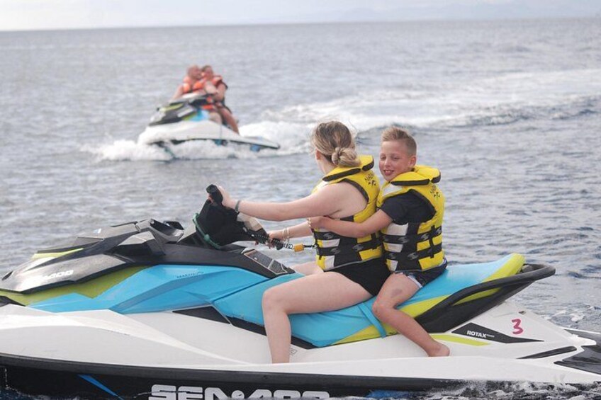 Two people on a jet ski wearing life jackets, with another jet ski in the background. 3