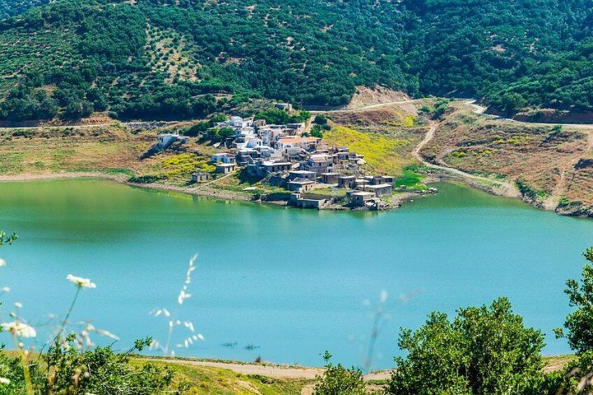 Un pueblo a orillas de un lago, con edificios agrupados junto a la orilla, rodeado de colinas verdes. 4