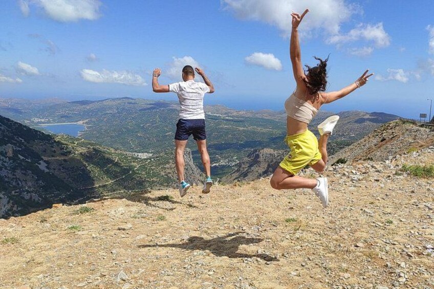 Dos personas saltan sobre una ladera rocosa con una vista panorámica de un valle y montañas al fondo. 3
