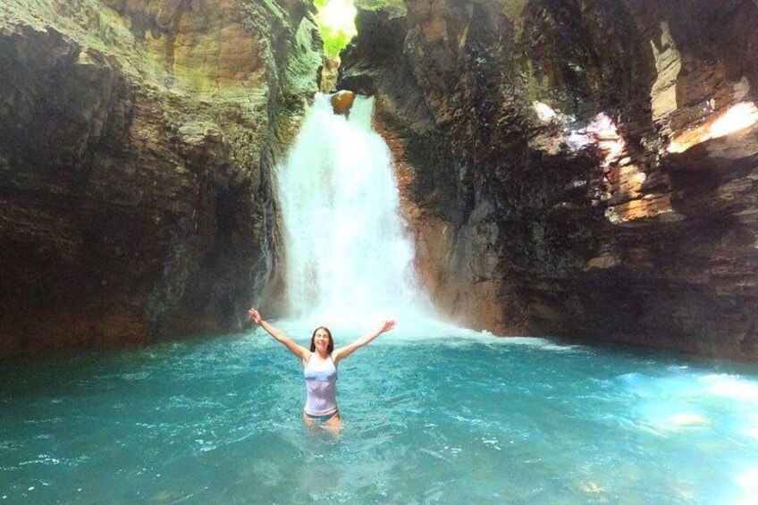 Une personne se tient dans l’eau, les bras levés, avec une cascade en arrière-plan et des falaises rocheuses. 3