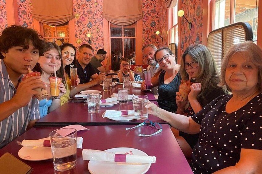 Un grupo de personas sentadas en una mesa en un restaurante con papel tapiz floral y mantel rojo. 4