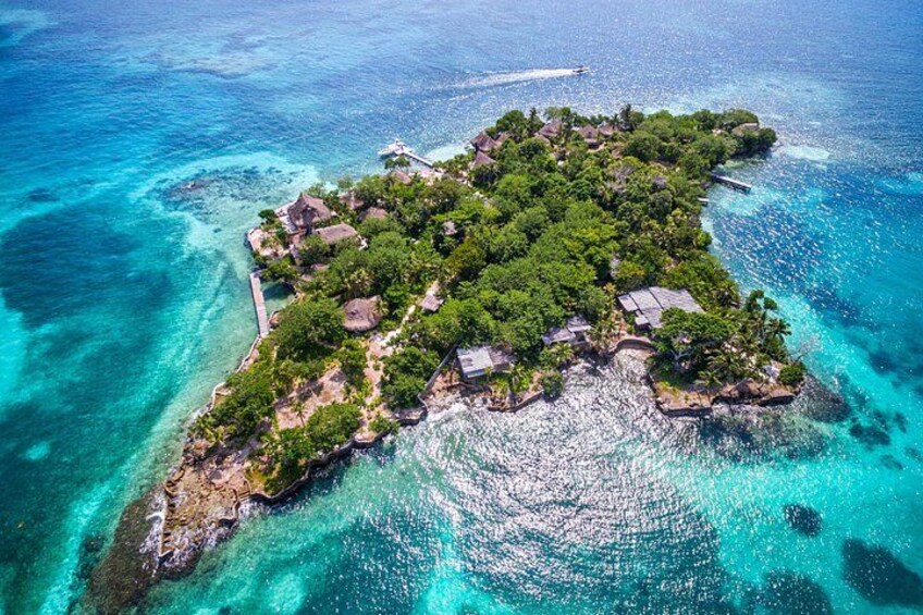 An aerial view of a tropical island with clear turquoise waters, lush greenery, and small buildings. 1