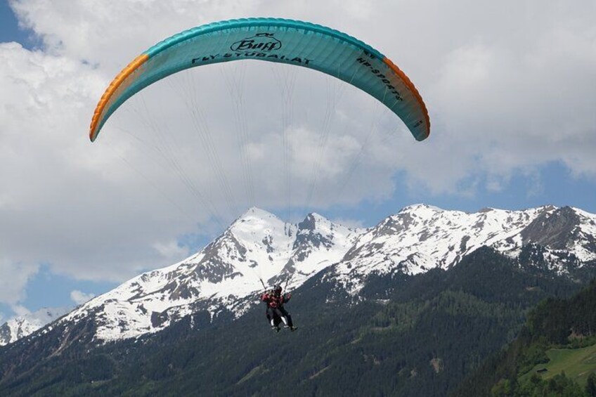 A paraglider with a blue and orange canopy flying over snow-capped mountains. 2
