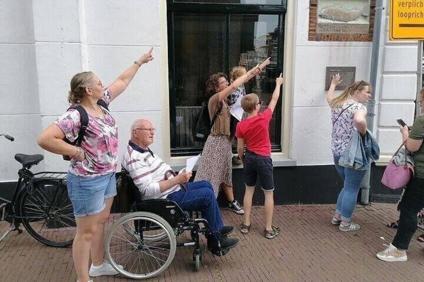 A group of people standing outside a building, some pointing towards the building. 3