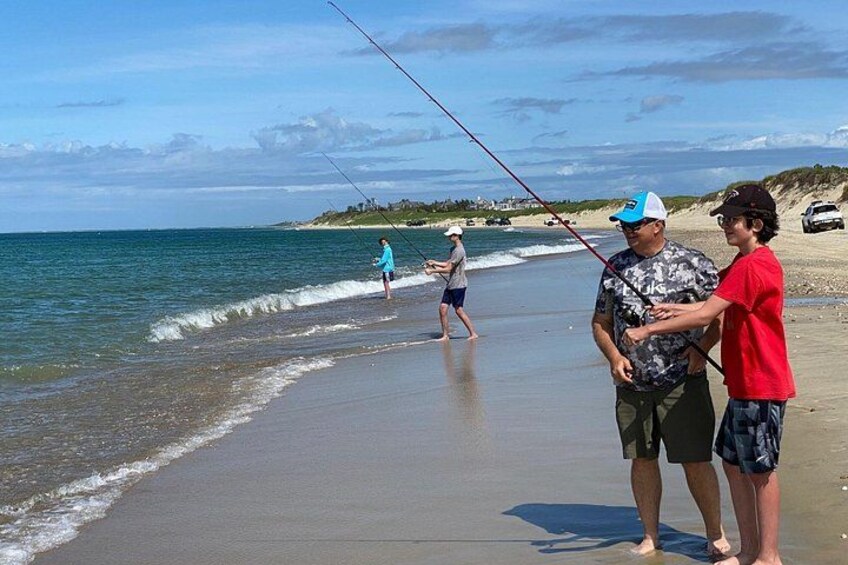 En strand med folk som fiskar, vågor och en avlägsen kustlinje. 4
