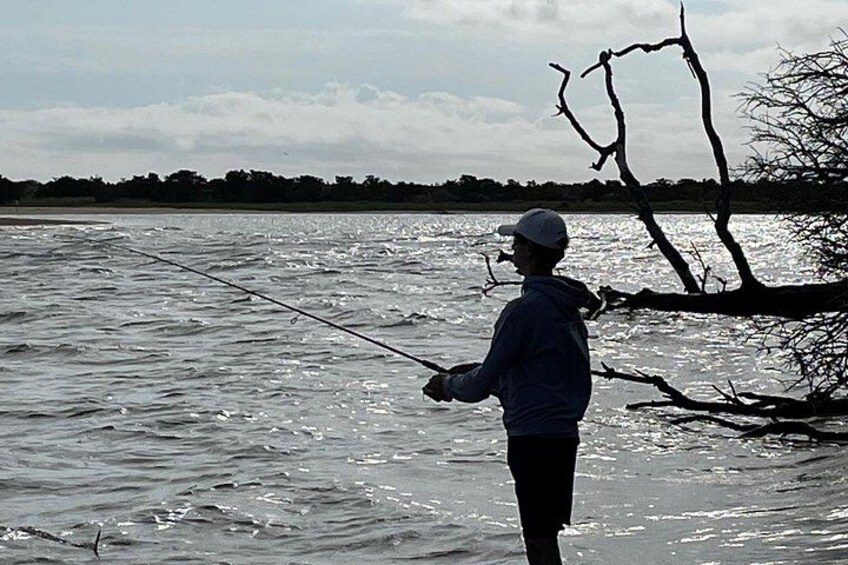 En person som fiskar vid ett vattendrag, med en trägren i förgrunden. 5