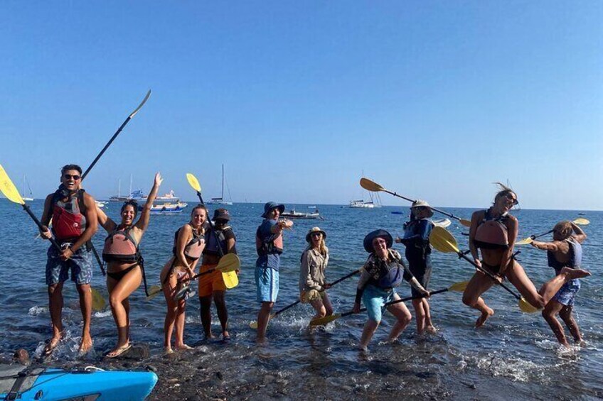 Eine Gruppe von Menschen paddelt mit Kajaks an einem Strand, im Hintergrund liegen Boote und Yachten. 3