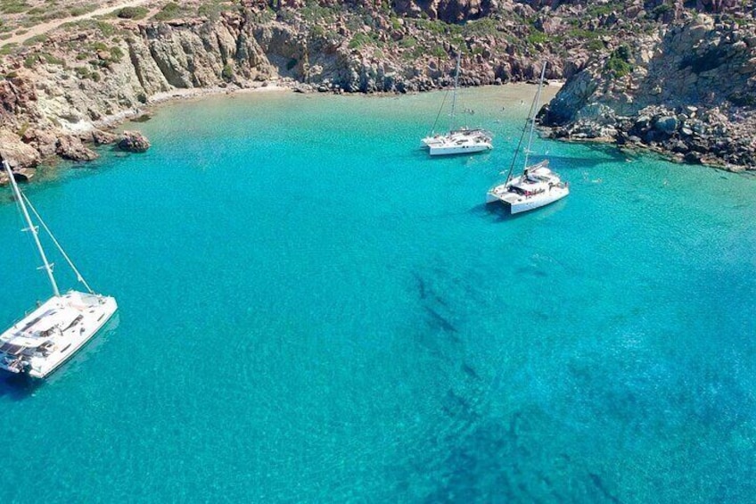 Tres veleros anclados en una bahía turquesa rodeada de acantilados rocosos. 1